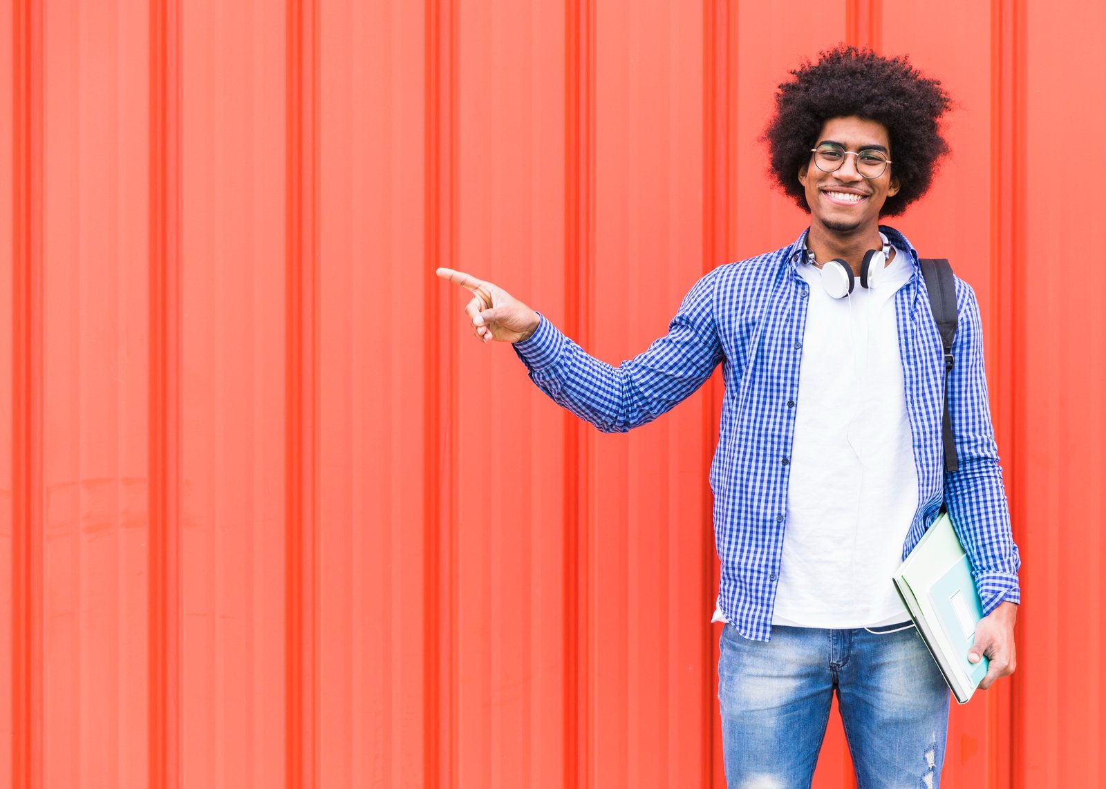 happy-portrait-male-student-pointing-his-finger-standing-against-bright-wall